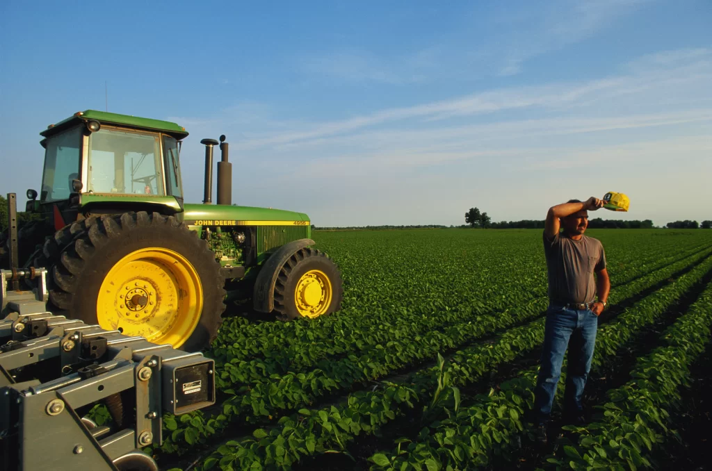 agricultor limpa testa em frente a trator no campo