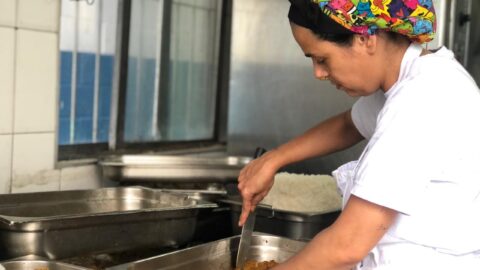 cozinheira mexendo em uma panela numa cozinha profissional