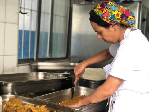 cozinheira mexendo em uma panela numa cozinha profissional